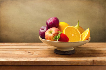 Vase with fresh fruits on wooden table