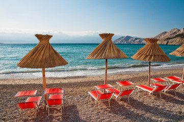 Sunshades and orange deck chairs on beach at Baska - Krk - Croat