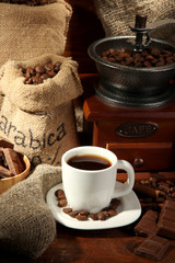 Coffee grinder and cup of coffee on brown wooden background