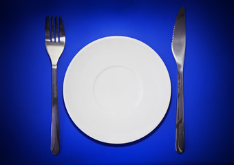 Table serving-knife,plate,fork on colour backdrop.