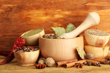 mortar, bowls and spoons with spices, on wooden background