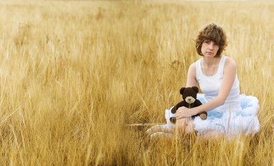 Naklejka na ściany i meble The sad girl in the field with a bear in a hand