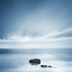 Des roches sombres dans un océan bleu sous un ciel nuageux par mauvais temps.