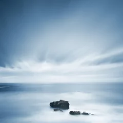 Fototapete Meer / Ozean Dunkle Felsen in einem blauen Ozean unter bewölktem Himmel bei schlechtem Wetter.