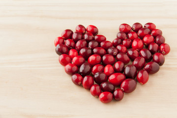 Cranberries in heart shape on wooden board.