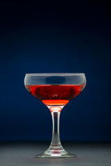 Glass filled with red wine over dark blue background.