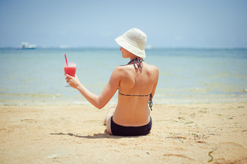 relaxing woman sitting on sand with cocktail 