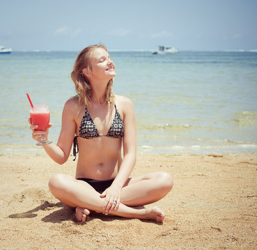relaxing woman sitting on sand with cocktail 