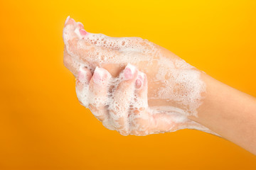 Woman's hands in soapsuds, on orange background close-up