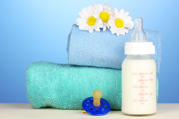 Obraz na płótnie Canvas Butelek mleka z smoczka i ręczniki na niebieskim tle