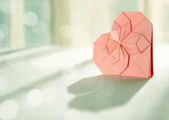 Sunlit pink origami paper heart with shadow