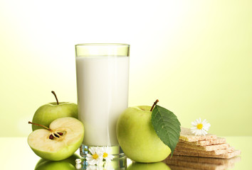 Glass of kefir, apples and crispbreads, on green background