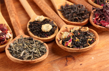 assortment of dry tea in spoons, on wooden background