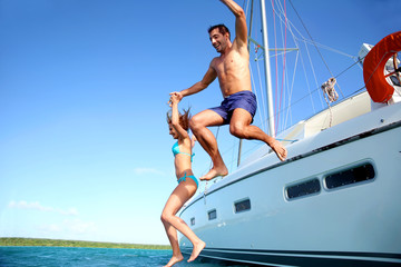 Young couple jumping in water from yacht - obrazy, fototapety, plakaty