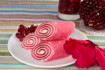 red candy fruit on a plate with pomegranate and flower