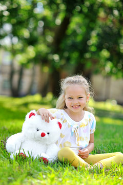 Adorable little girl with a toy bear in a park