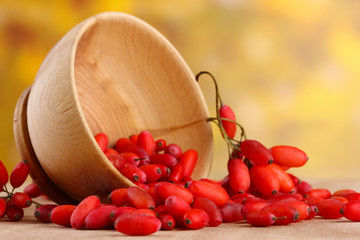 ripe barberries in wooden bowl, on table, on yellow background
