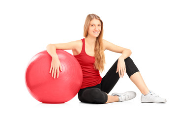 Young female athlete sitiing on a floor next to a pilates ball