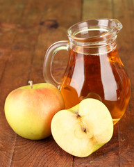 Full jug of apple juice and apple on wooden background