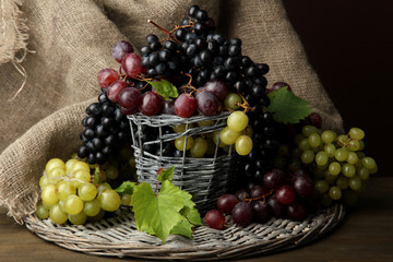 assortment of ripe sweet grapes in basket, on brown background