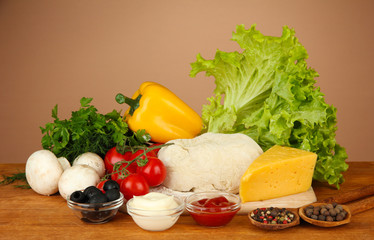 Ingredients for pizza on wooden table on brown background