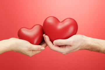 Red hearts in woman and man hands, on red background