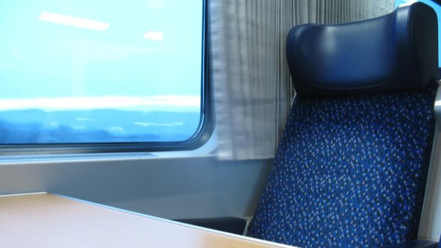 Empty dark blue armchair stands near window of moving train