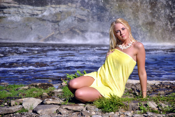 Young girl wrapped in towel sitting on a waterfall background