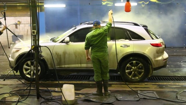Two workers wash car indoors strong streams of water