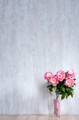 Bouquet of peonies in a vase against a blue wall. Interior.