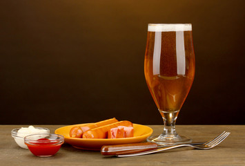 Beer and grilled sausages on wooden table on brown background