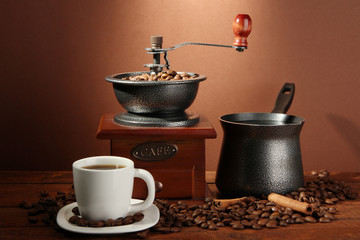 Coffee grinder, turk and cup of coffee on brown background
