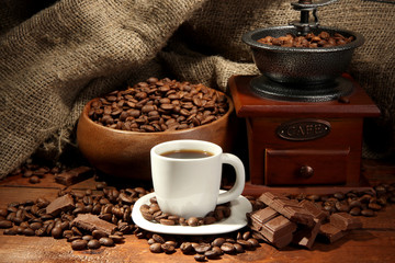 Coffee grinder and cup of coffee on burlap background