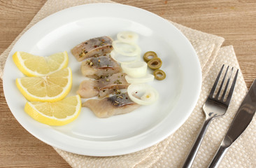 Dish of herring and lemon on plate on wooden table close-up