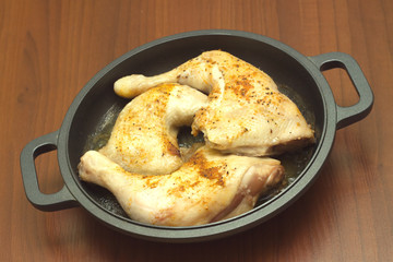 Fried appetizing chicken legs in black pan closeup