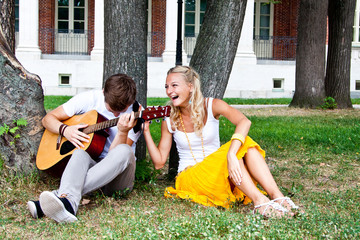 A young man plays guitar in the park beautiful woman