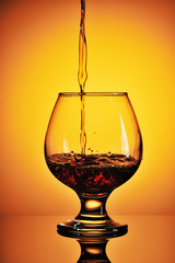 Pouring cognac in glass on a gold background