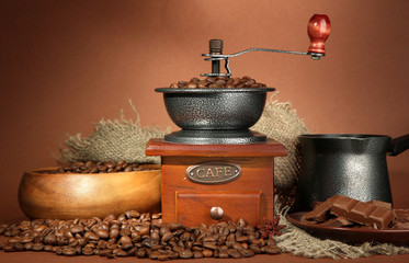 Coffee grinder, turk and coffee beans on brown background