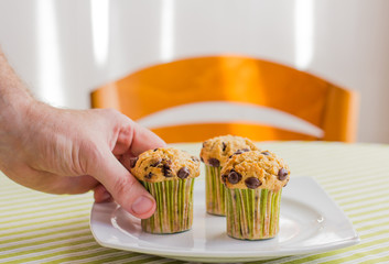 Man hand taking chocolate chip muffin at breakfast