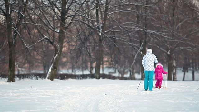 Mother and child running away on ski in park. Rear view