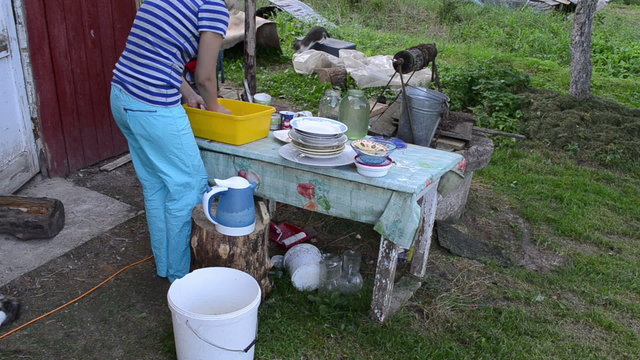 deprived woman wash dirty dishes and cats walk. rural poverty