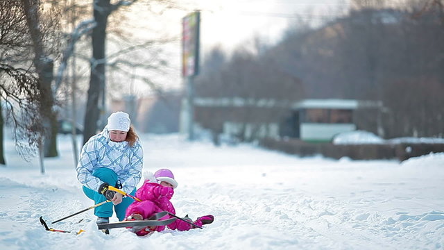 Mother helping little child to ski in city park in winter