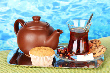 glass of Turkish tea and kettle on color background