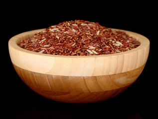 Red rice in wooden bowl isolated on black