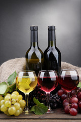 bottles and glasses of wine and grapes on grey background