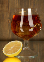 Glass of brandy with ice and lemon on wooden background