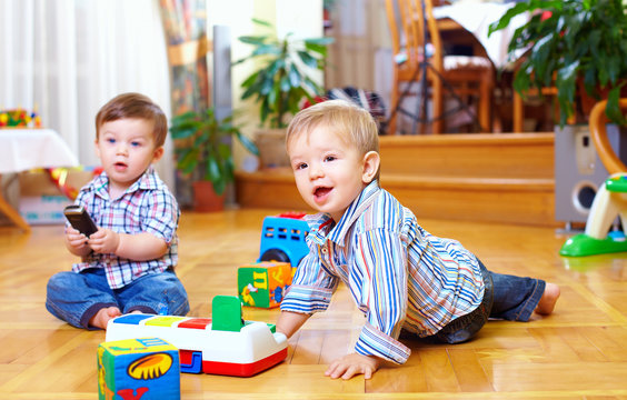 two cute baby boys playing with toys at home