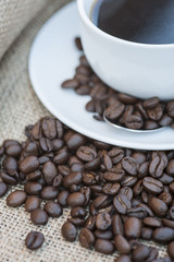 Close up of coffe cup and saucer surrounded by beans on hessian