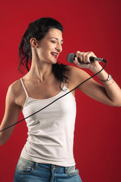 Beautiful girl singing with microphone against red background.