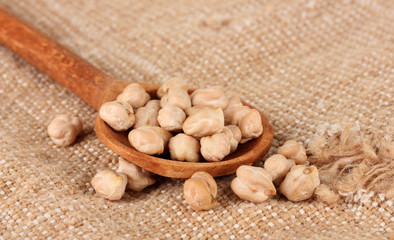 White chickpeas over wooden spoon on sackcloth background